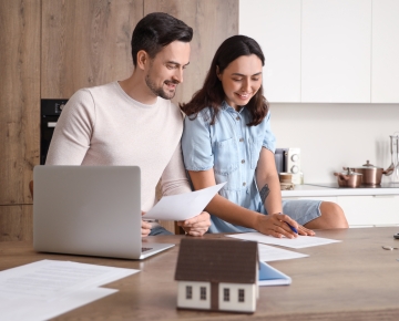 couple at kitchen counter looking at laptop and papers