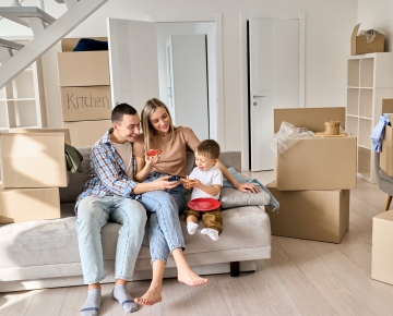 couple and son sitting on couch in new home with boxes in background