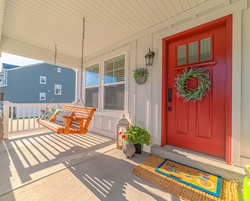 front porch with red door, swing, door mats, and plants