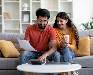 couple sitting on couch using calculator and holding paper
