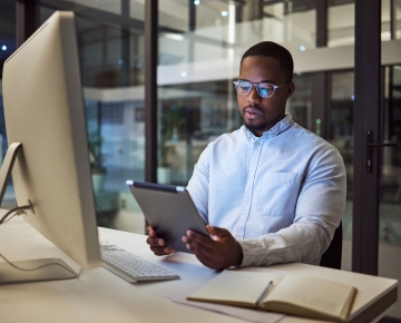man in office looking at tablet with computer in front of him